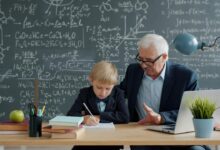 Elderly man teaching young boy math at desk.