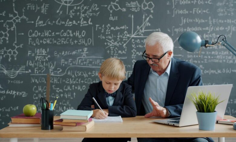 Elderly man teaching young boy math at desk.